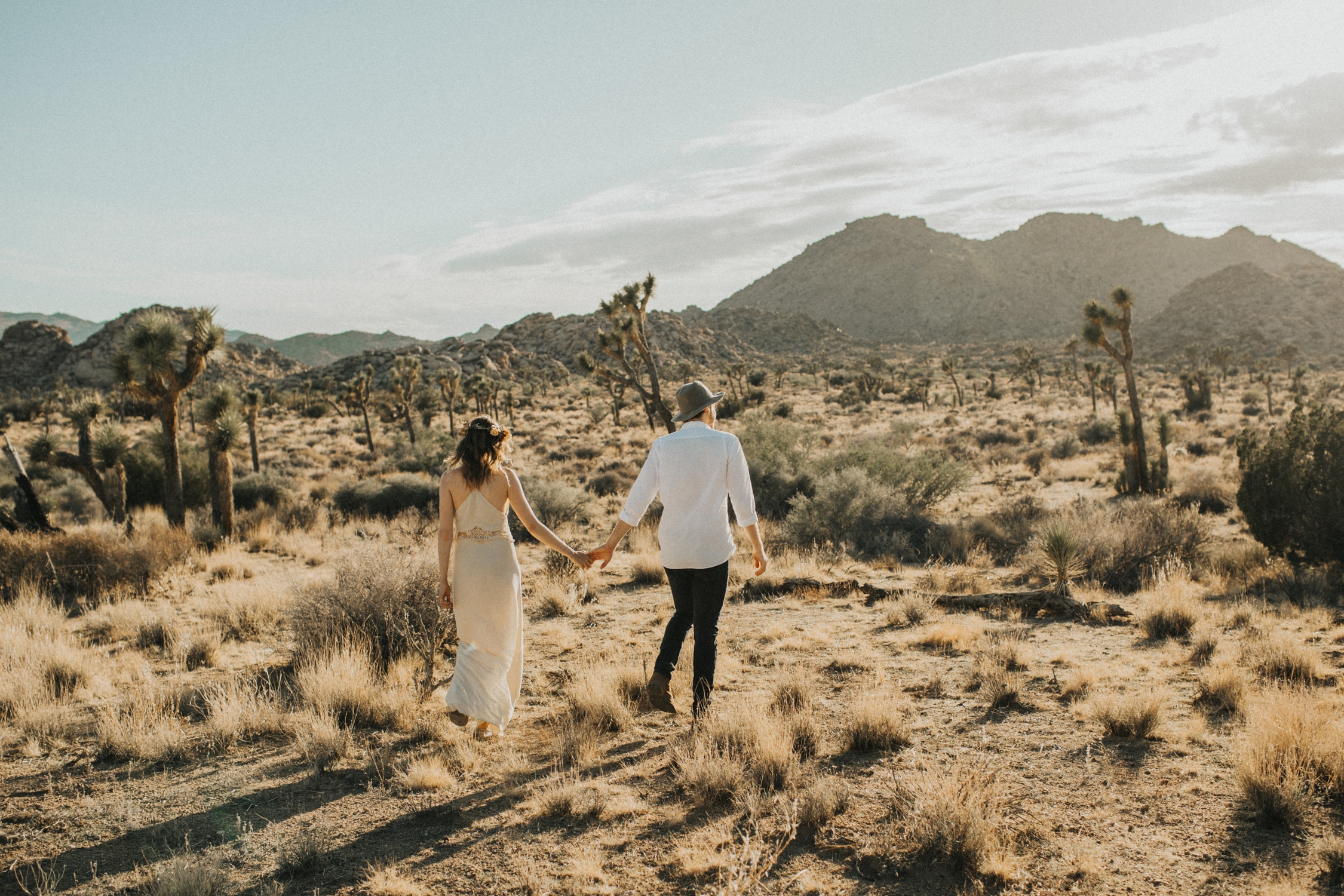 A couple is walking, holding hands, during their elopement in Joshua Tree National Park.
