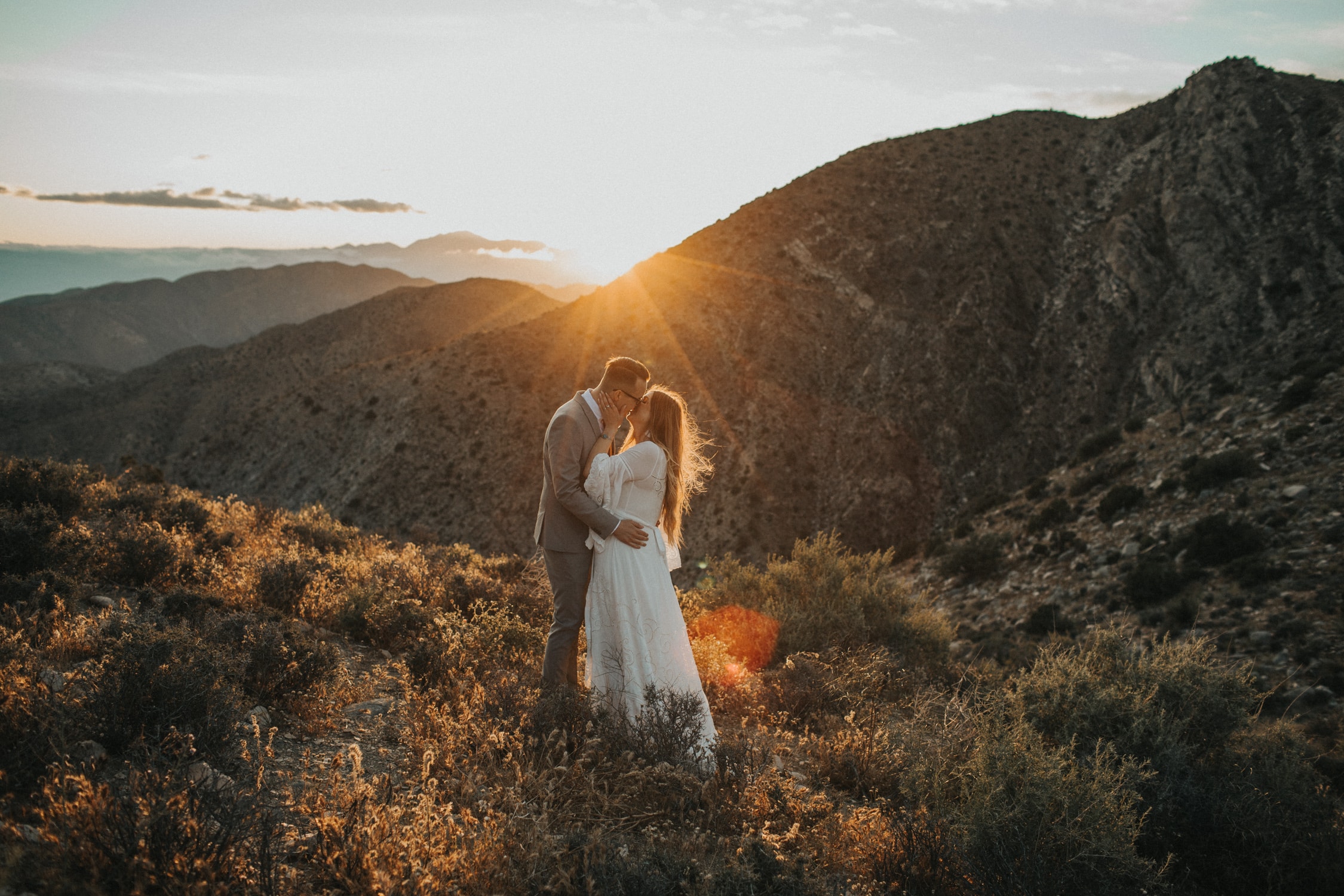 A couple is standing in front of a sunset in the mountains during their elopement in Joshua Tree National Park.